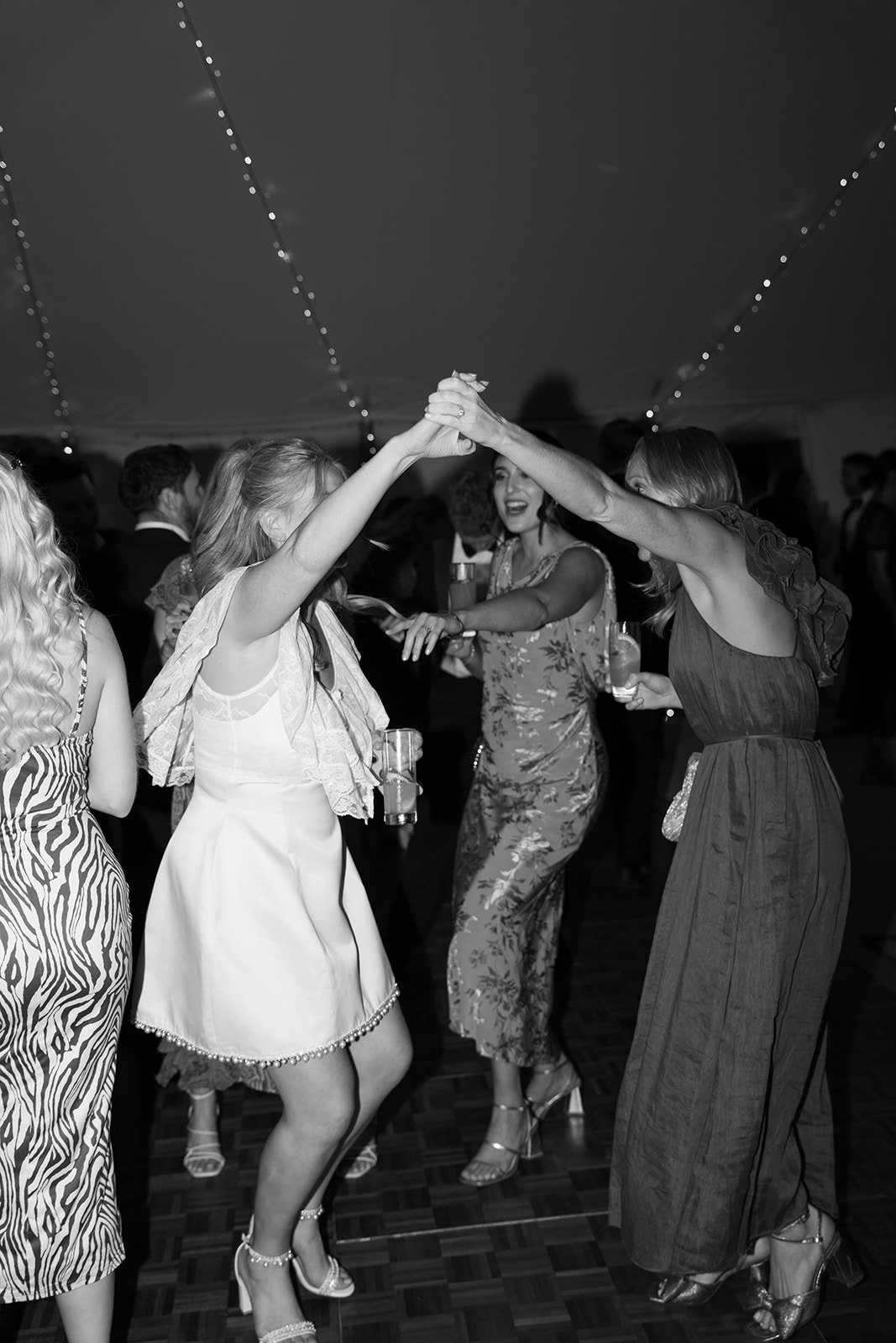 People dancing and celebrating at a party under string lights, black and white photo.