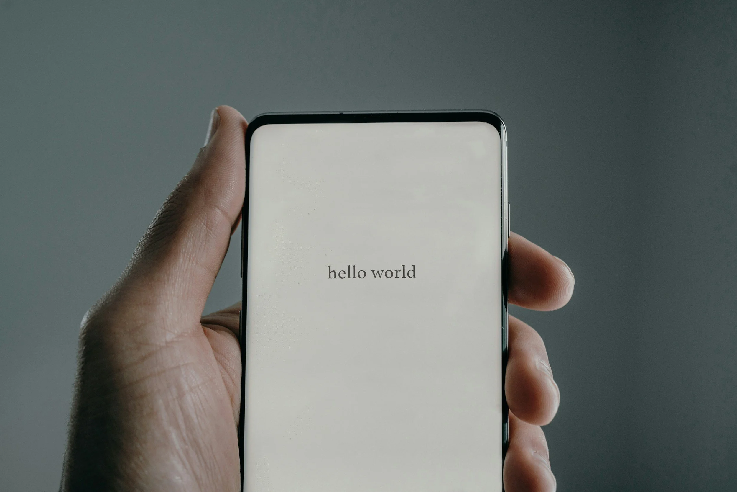 mans hand holding phone with the word hello world