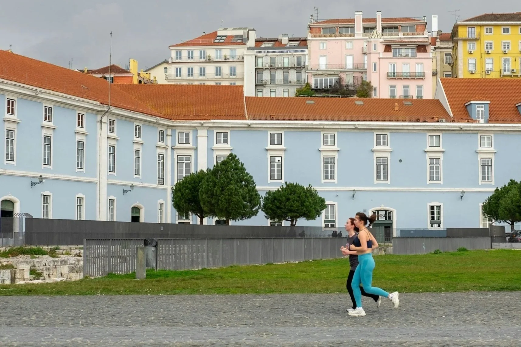 Two girls running in Lisbon along the waterfront in front of a blue building