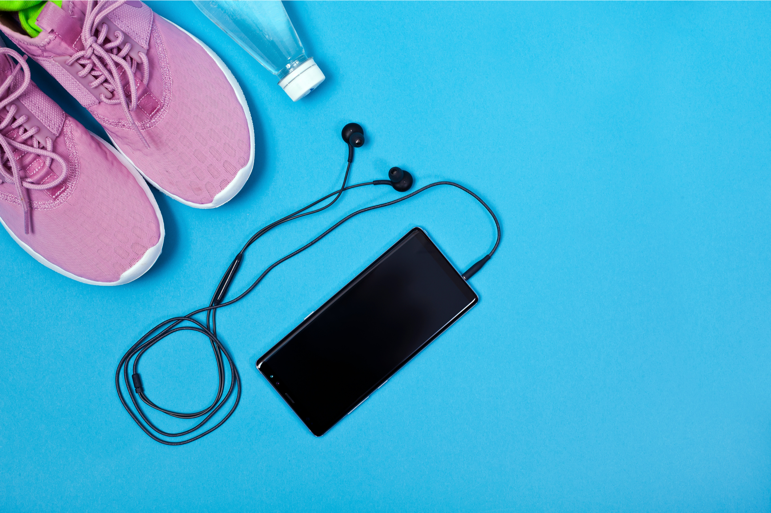 Pink running shoes, a water bottle and a phone with headphones on a blue background