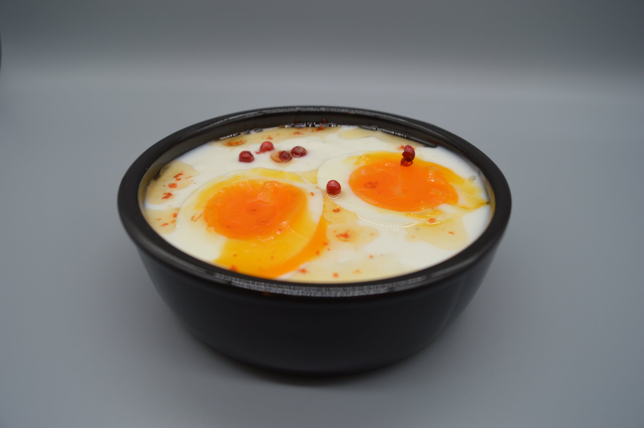 Kom gevuld met gekookte eitjes, Griekse yoghurt, olijfolie, harissa en peperbolletjes