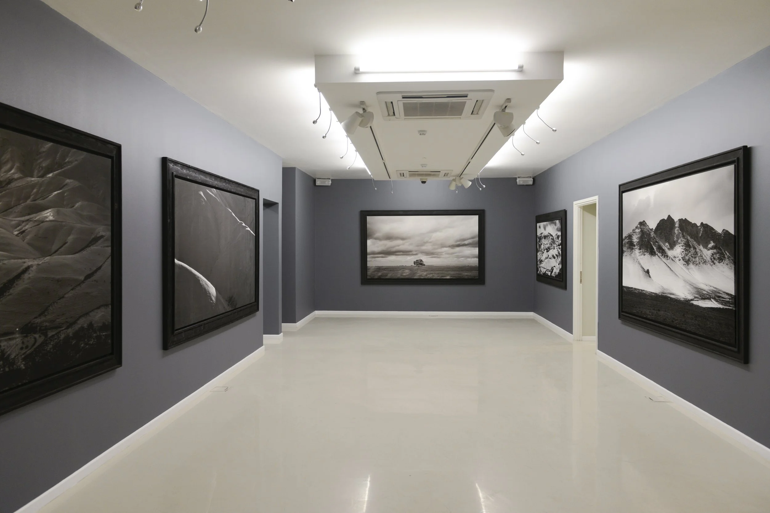 An art gallery with dark gray walls and black-and-white landscape photographs framed in black, displayed in a minimalistic, well-lit room.