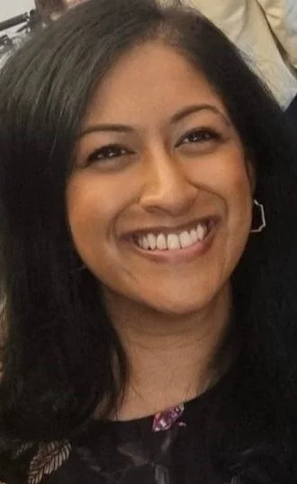 Close-up of a smiling woman with black hair and earrings.