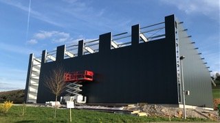 Modern black building with a red fire escape and a blue sky background.