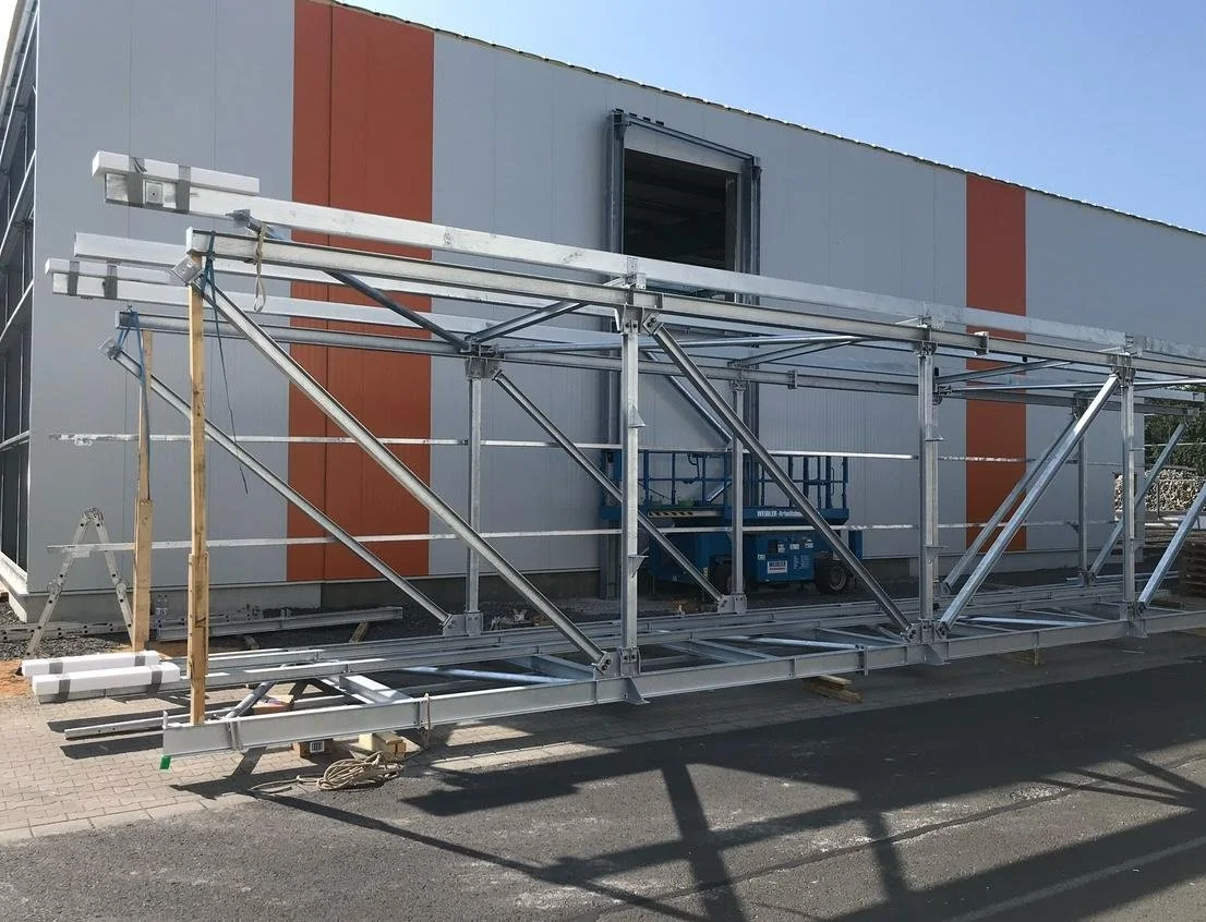 Metal scaffolding structure in front of a gray building with orange vertical stripes, with an open window above.