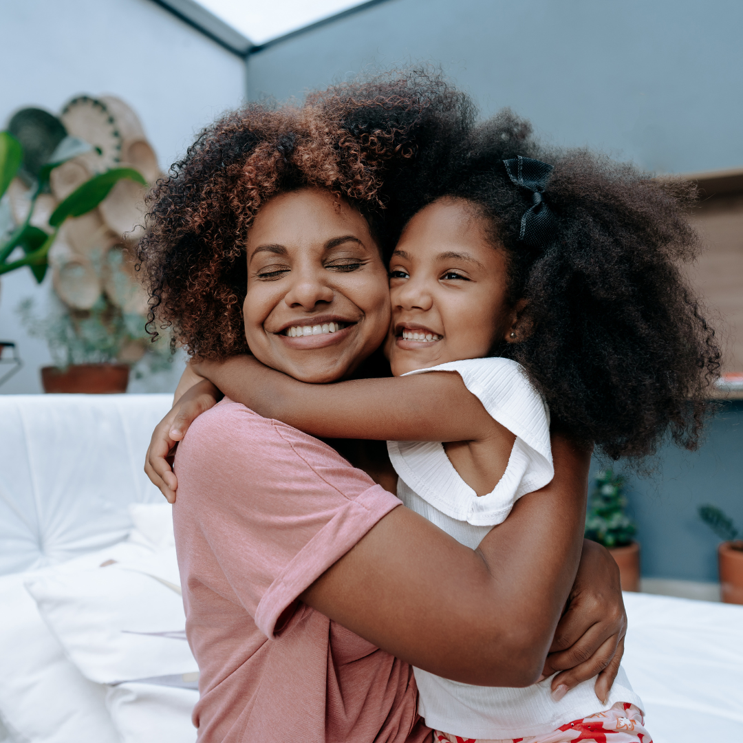A woman and a young girl hugging and smiling happily.