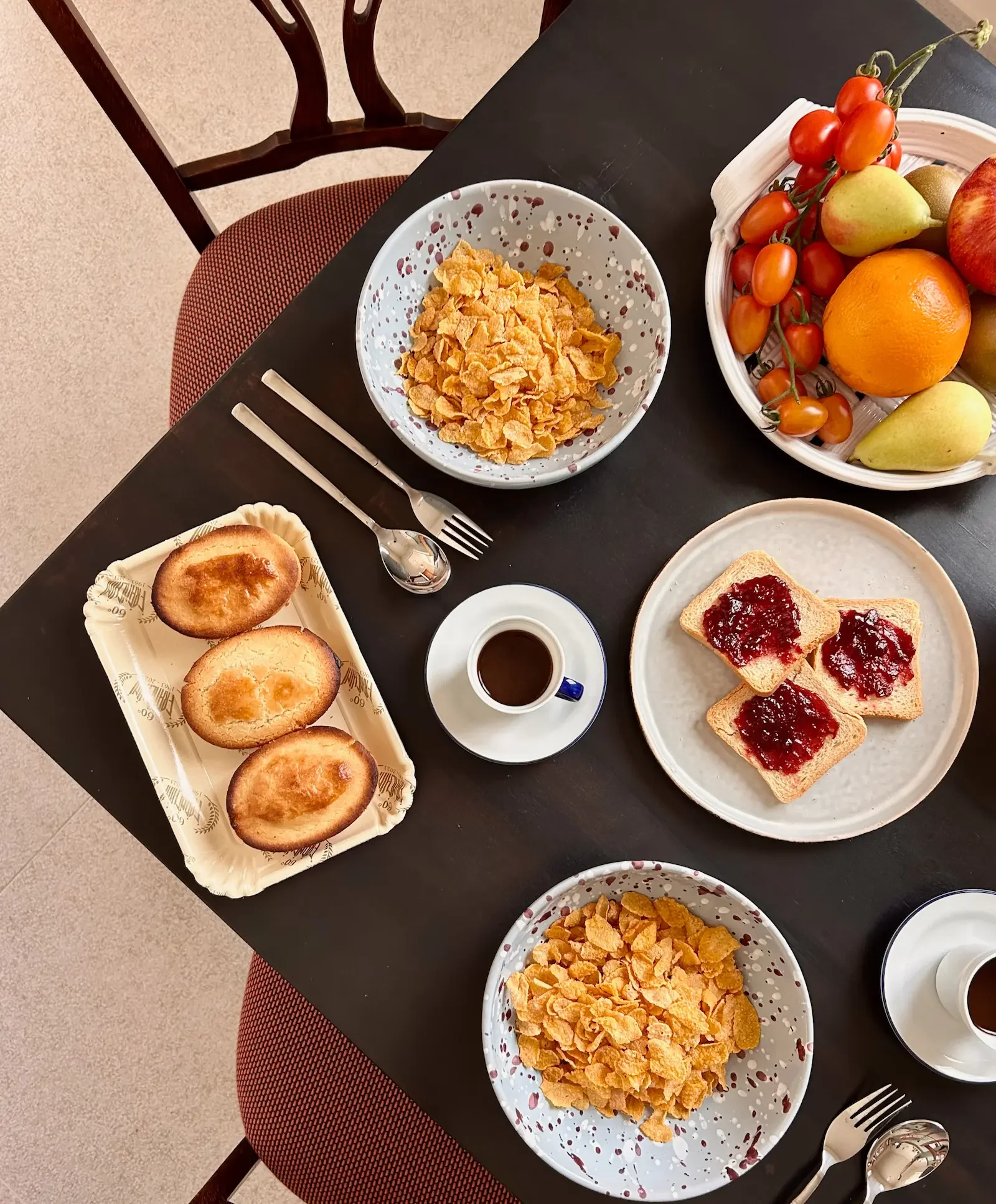 Breakfast table with cereal, pasticciotto, Italian pastries, toast with jam, coffee, fresh fruit, and berries. Splatter plates by Enza Fasano, coffee cups by Richard Ginori