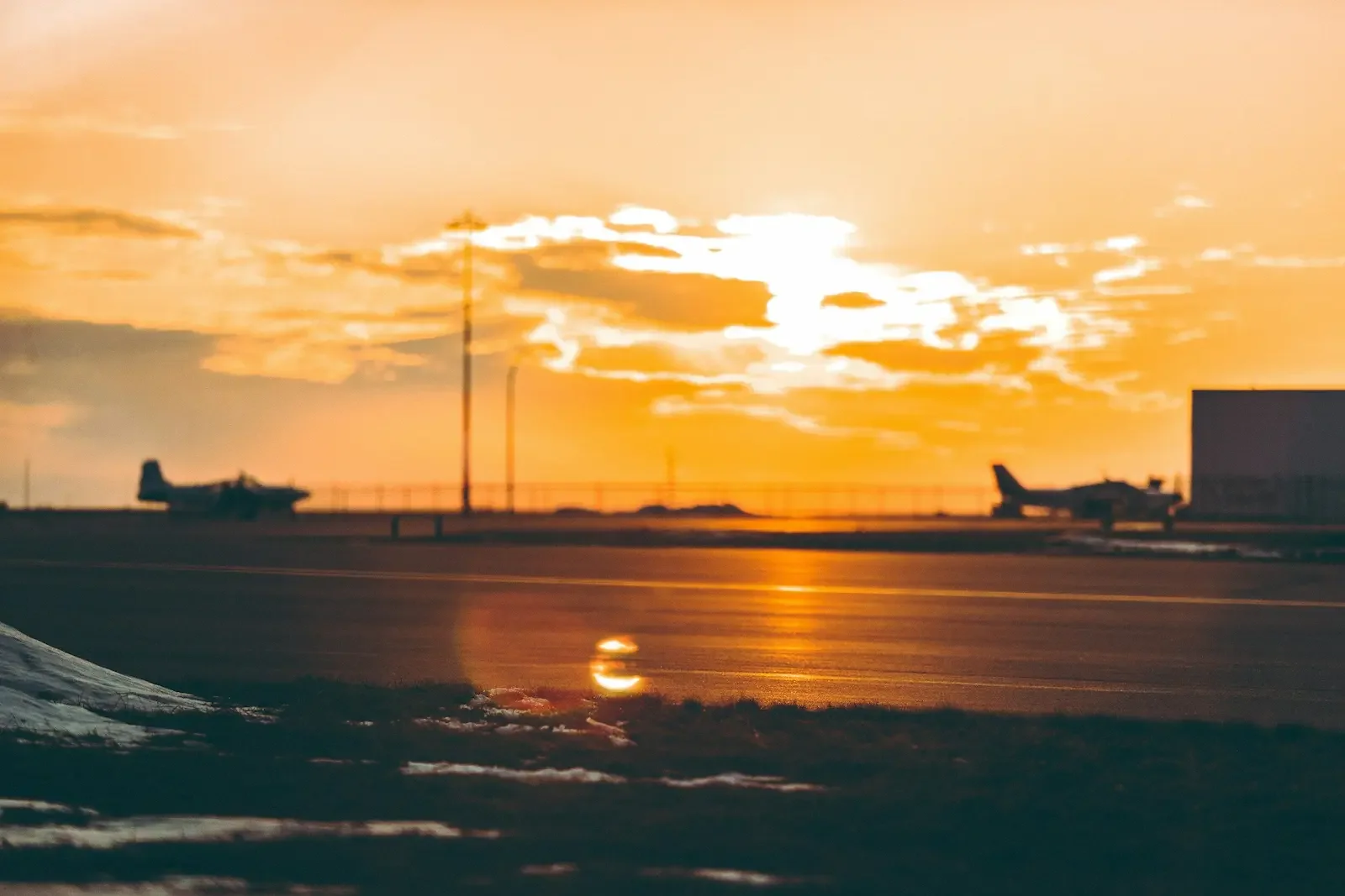 Two planes parked on an airport runway during sunset with golden sky and clouds.
