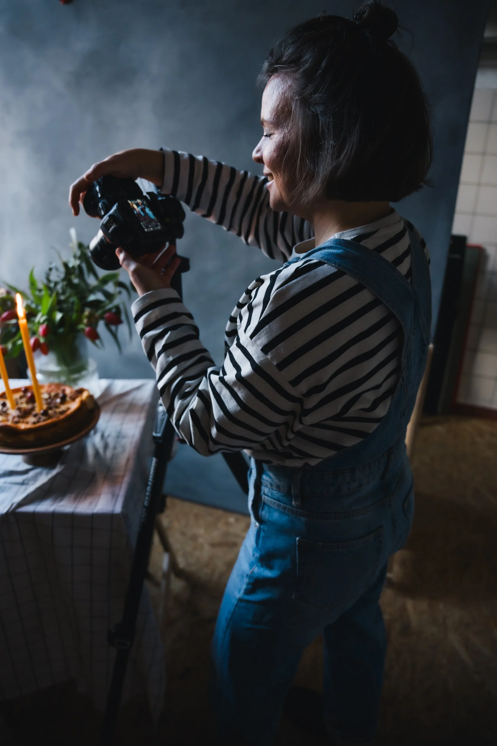 Frau macht Fotos von einem Geburtstagskuchen mit Kerzen auf einem Tisch.
