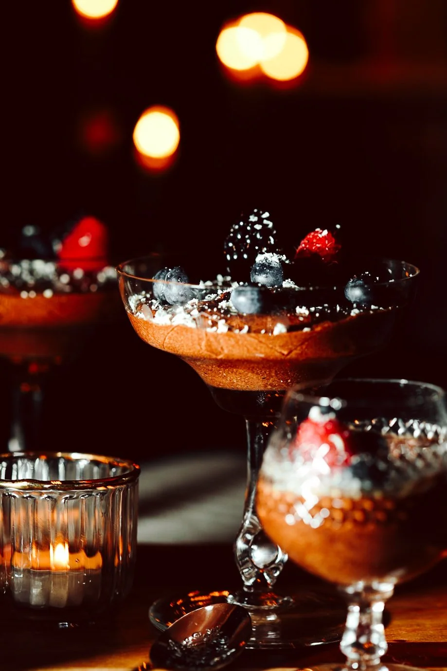 Dessert im Glas mit Schokolade, Beeren und Kokosnussflocken, dekoriert mit Beeren, vor warmem Kerzenlicht.