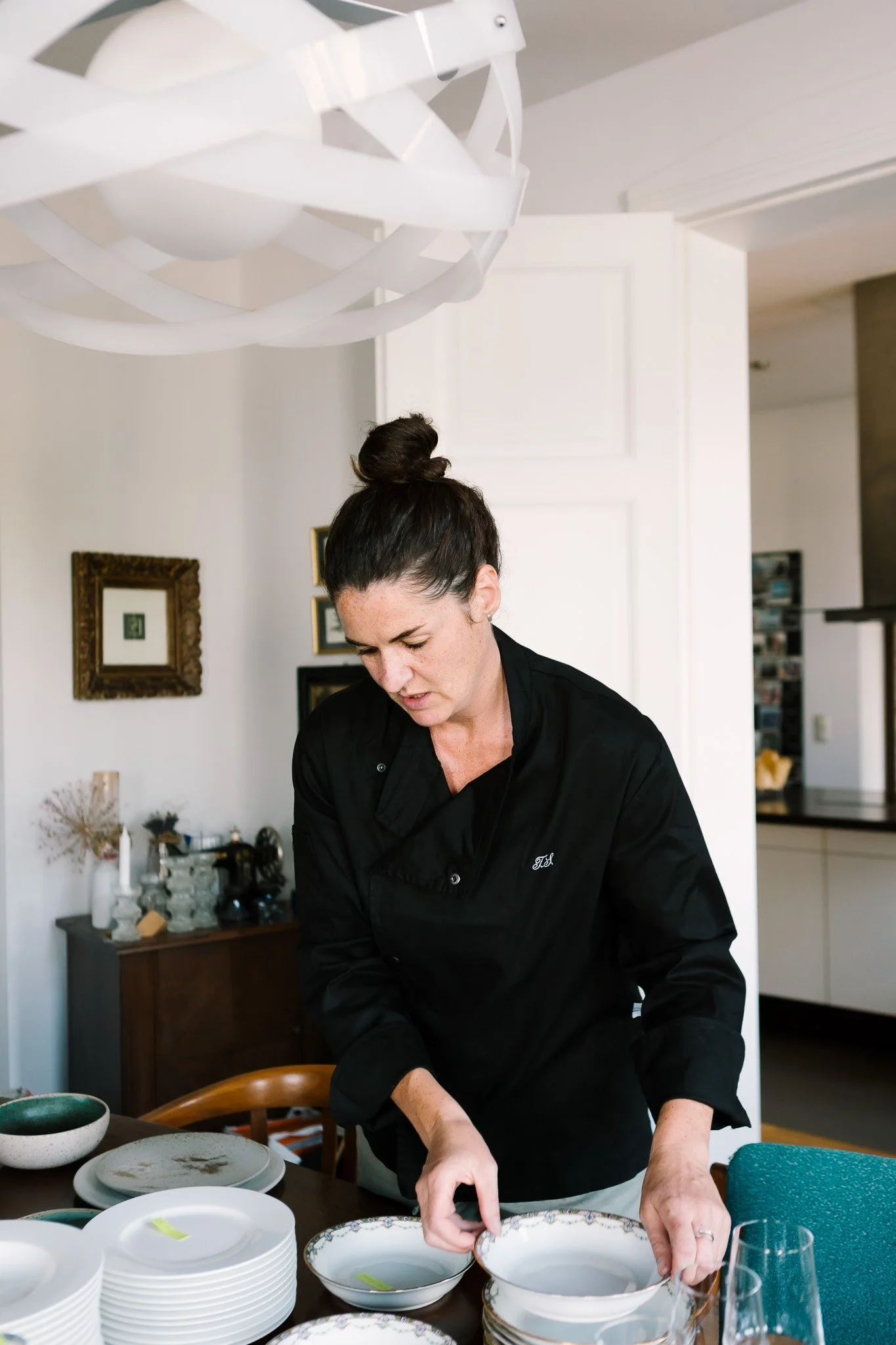 Frau in schwarzem Kochoutfit beim Abwaschen von Geschirr in einer modernen Küche.