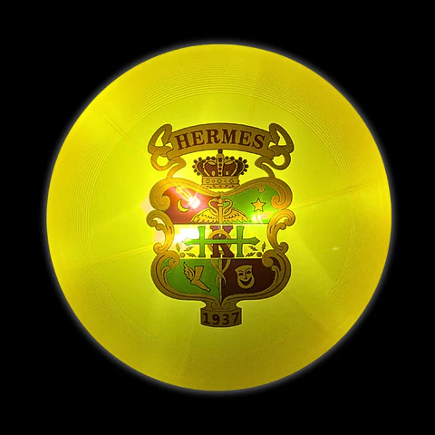 Yellow circular lamp with a Hermès logo featuring a crest with a crown, various symbols, and the year 193
