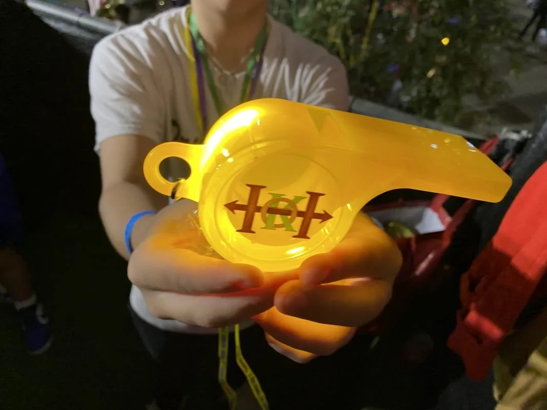 A person holding a yellow plastic souvenir with a merlin bird silhouette and the text 'H' and 'R' inside it.