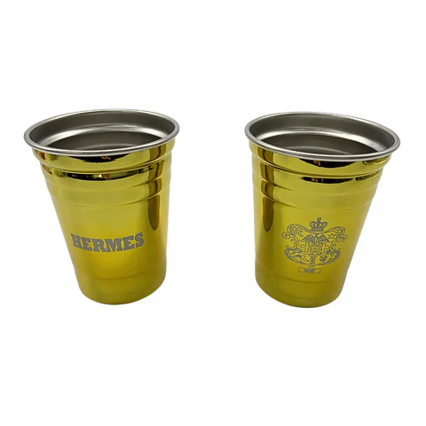 Two metallic gold-colored cups with silver rims, each featuring different logos, placed side by side.