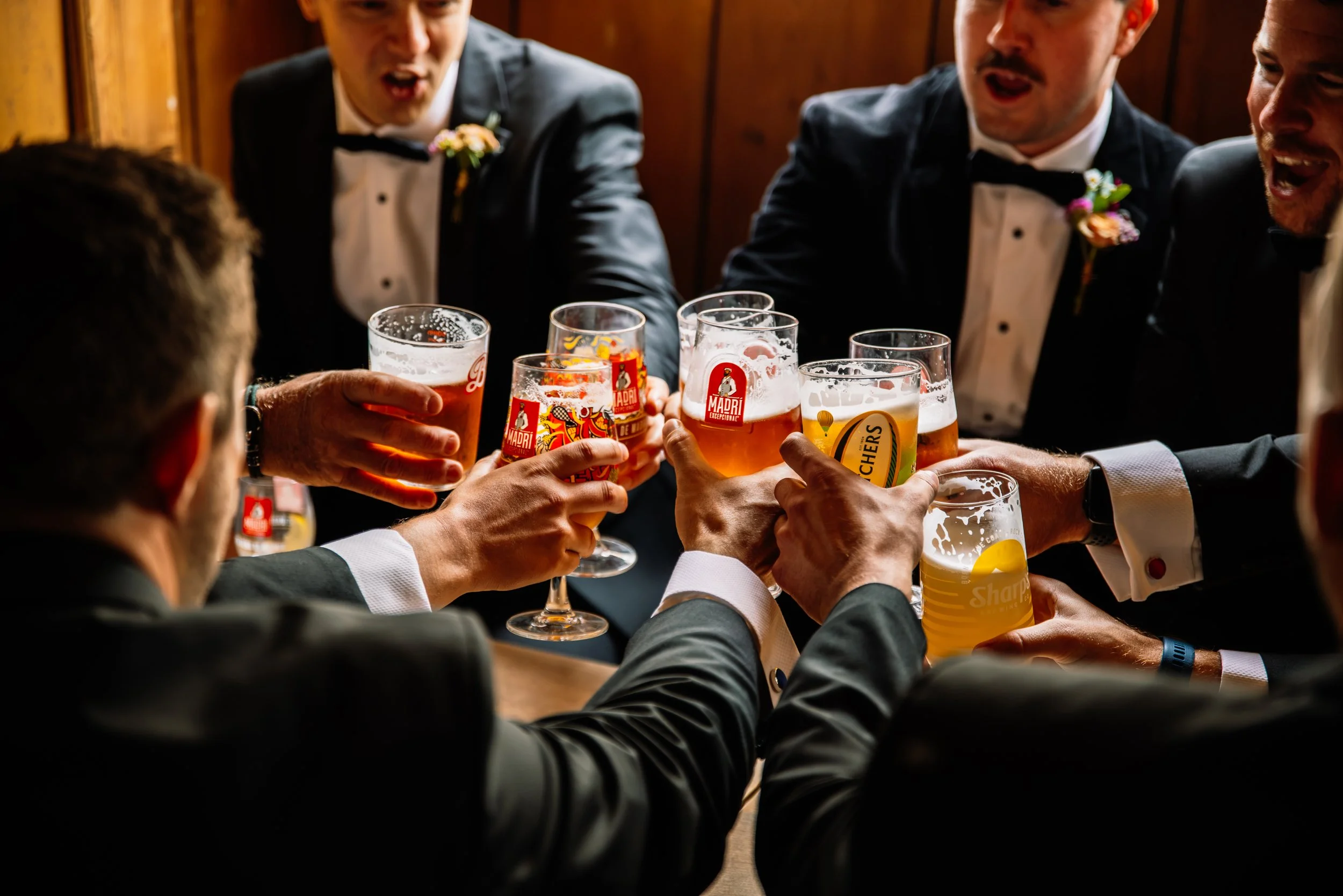 A group of men in tuxedos clinking glasses of beer at a celebration.