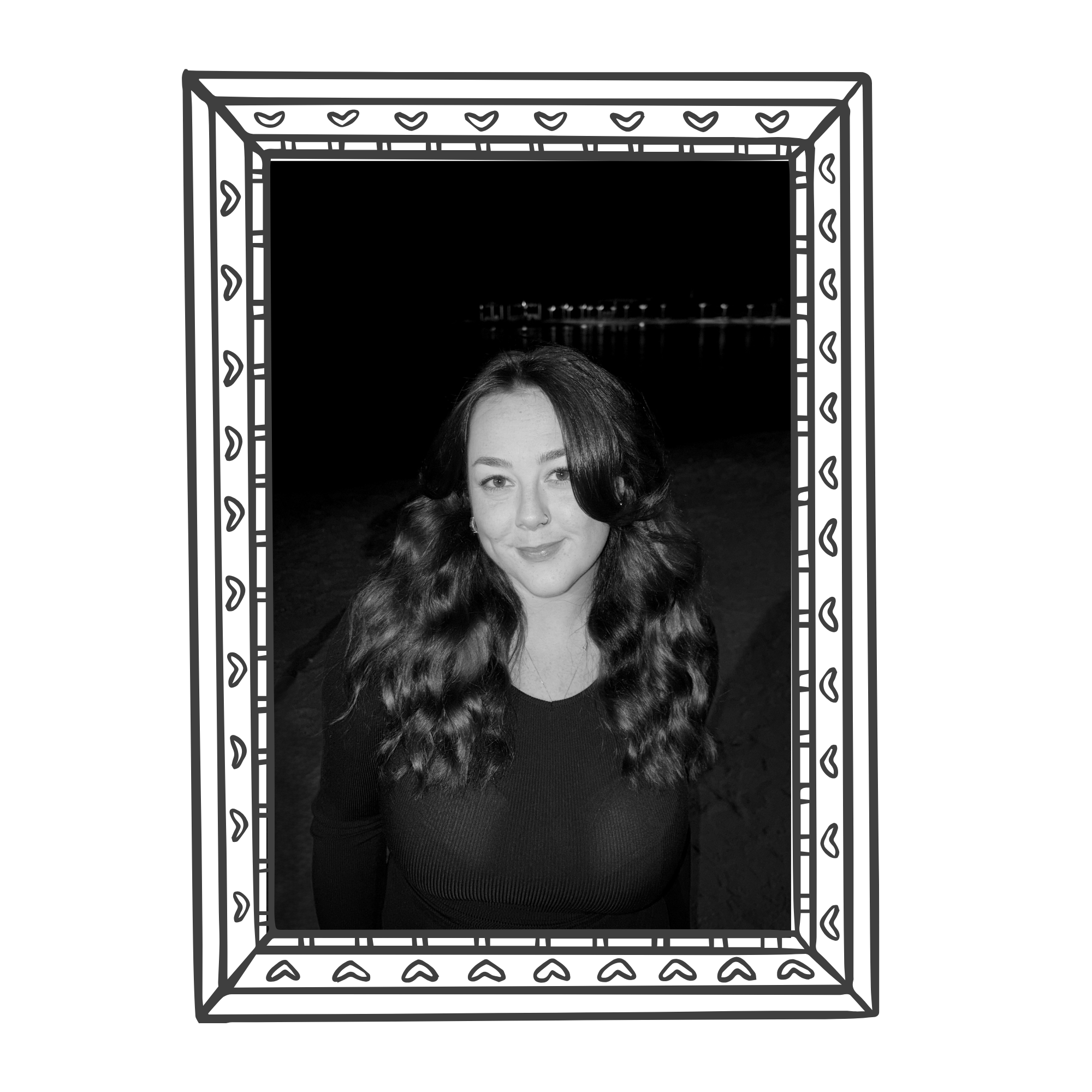 Black and white photo of a woman with long, wavy hair smiling outdoors at night, framed in a decorative picture frame.