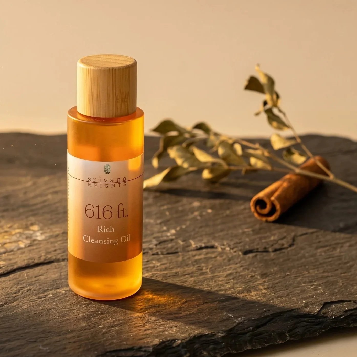 A bottle of Srivana Heights 616 ft. rich cleansing oil on a wooden surface with dried leaves and a cinnamon stick in the background.