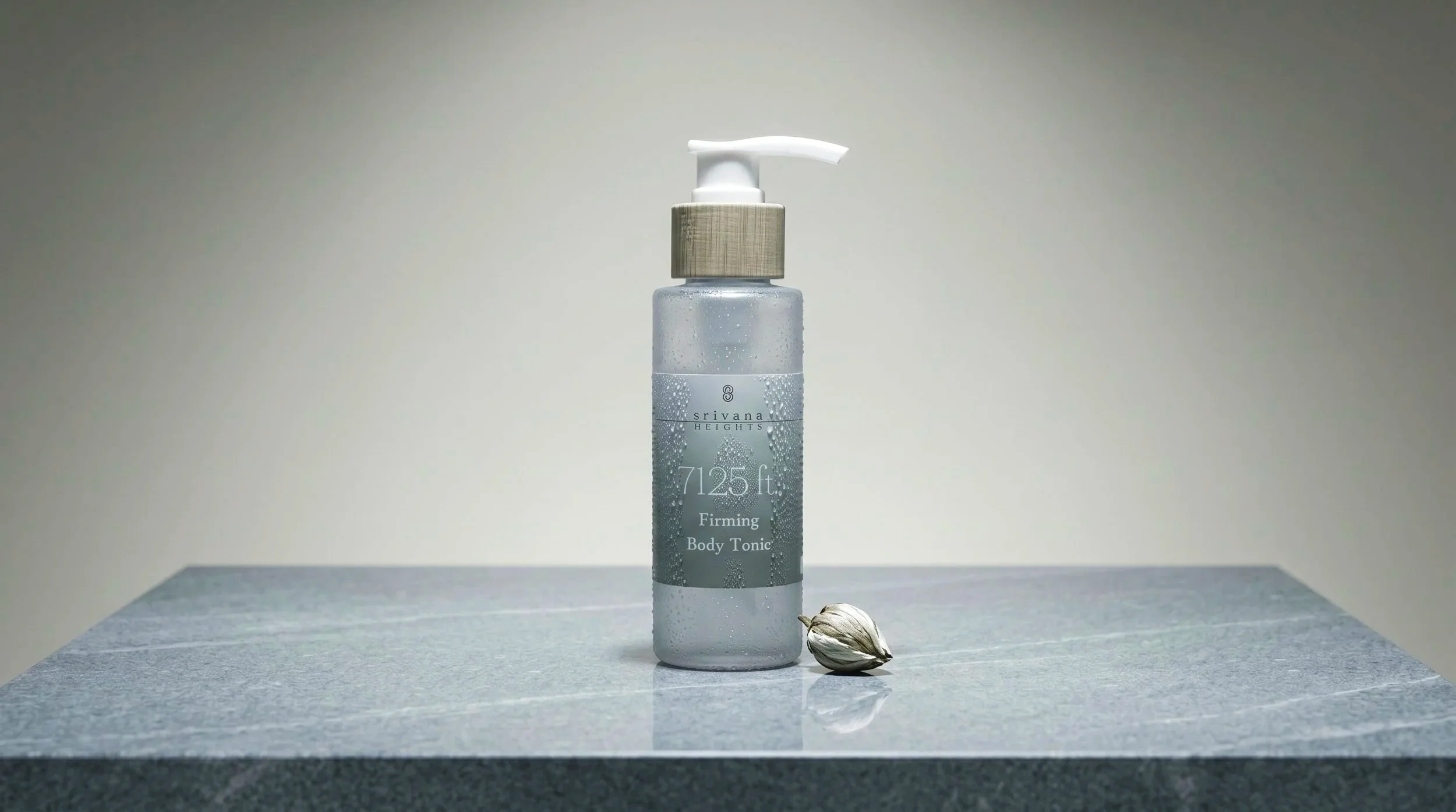 A clear plastic spray bottle labeled 'Srivana Heights 7125 ft Firming Body Tonic' on a textured surface, with a garlic bulb in front, against a neutral background.