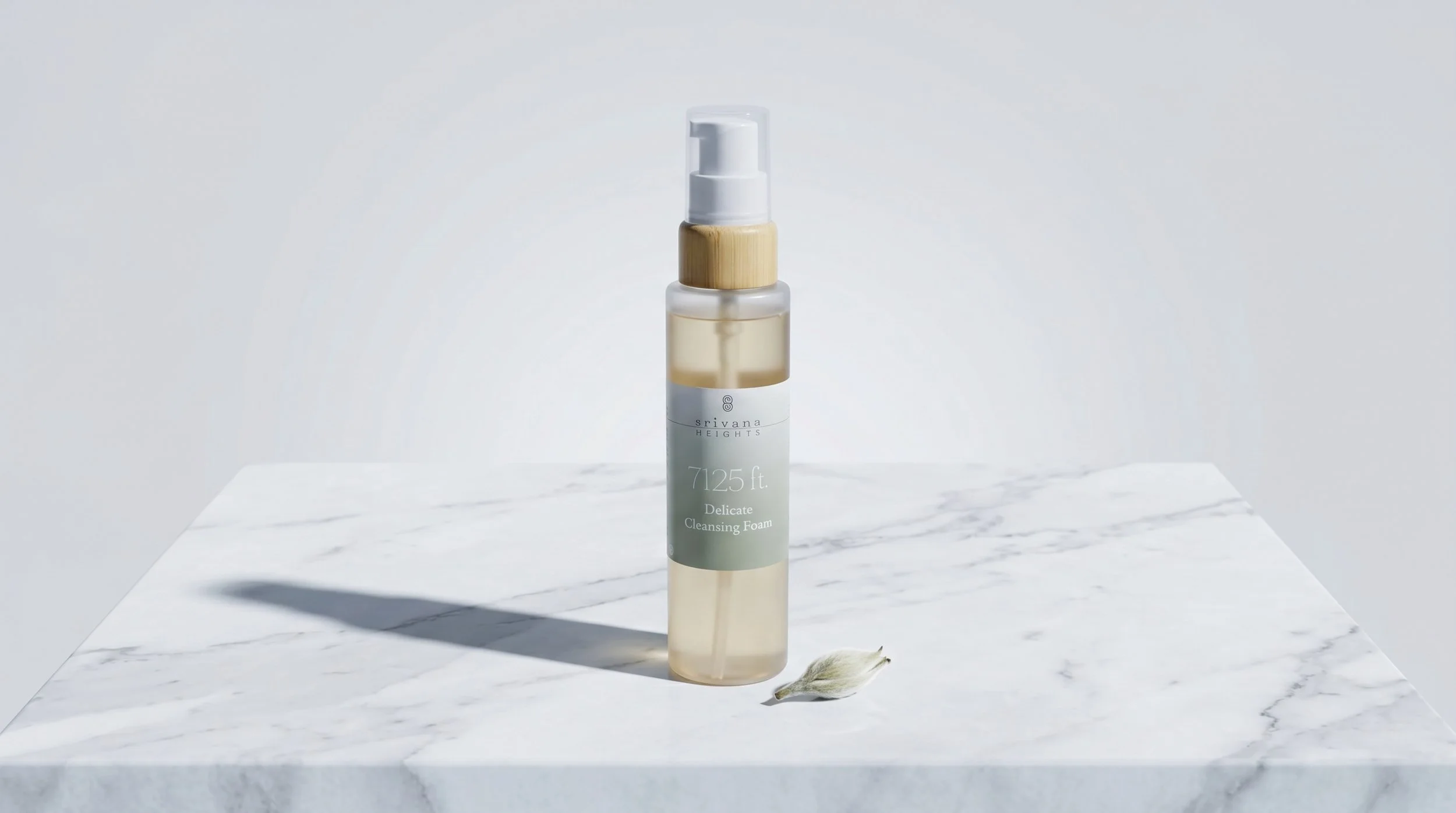 A bottle of Srivana Heights Delicate Cleansing Foam on a white marble surface, with a white background and a soft shadow.