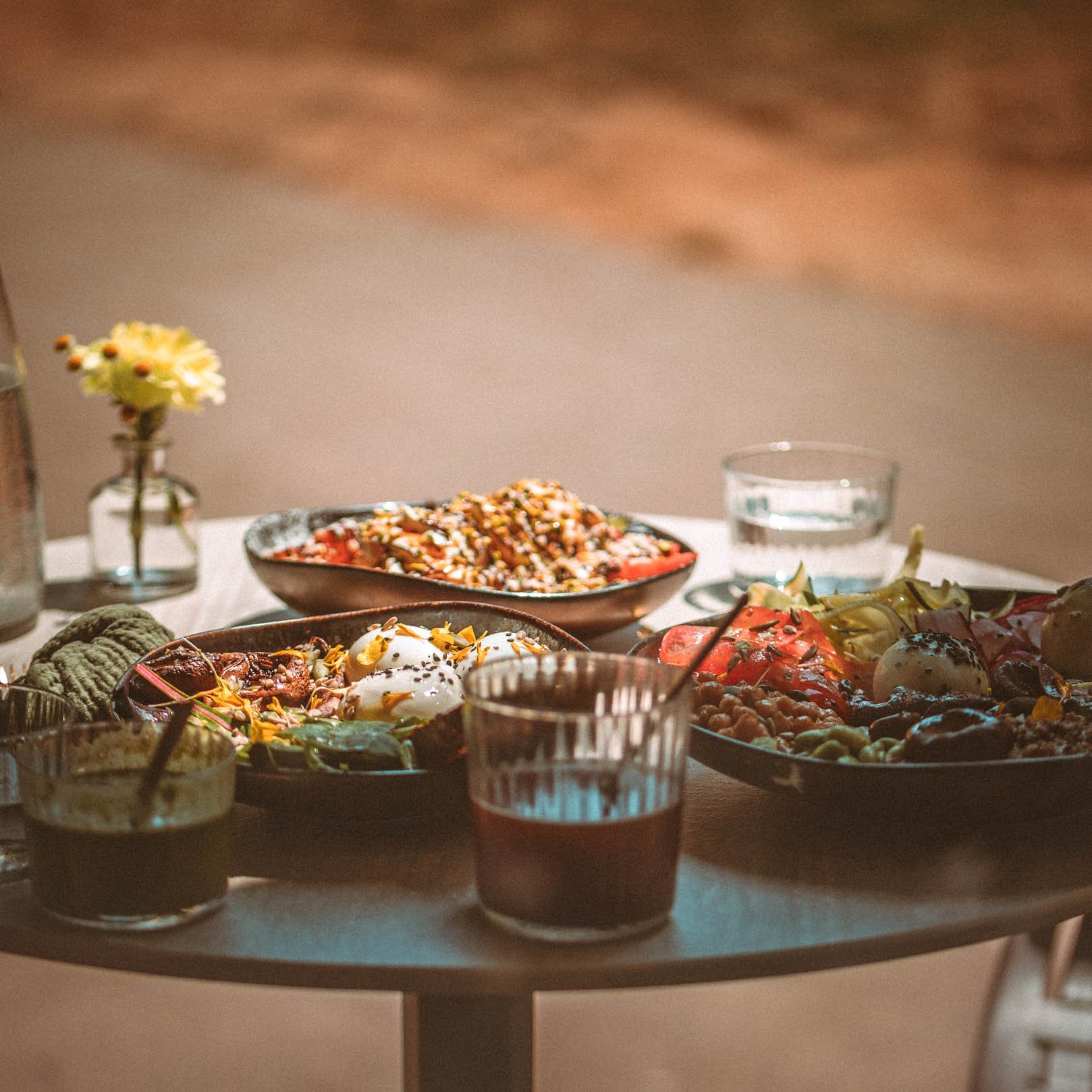 Table avec diverses assiettes de nourriture, verres d'eau, et une petite vase avec une fleur, ambiance chaleureuse