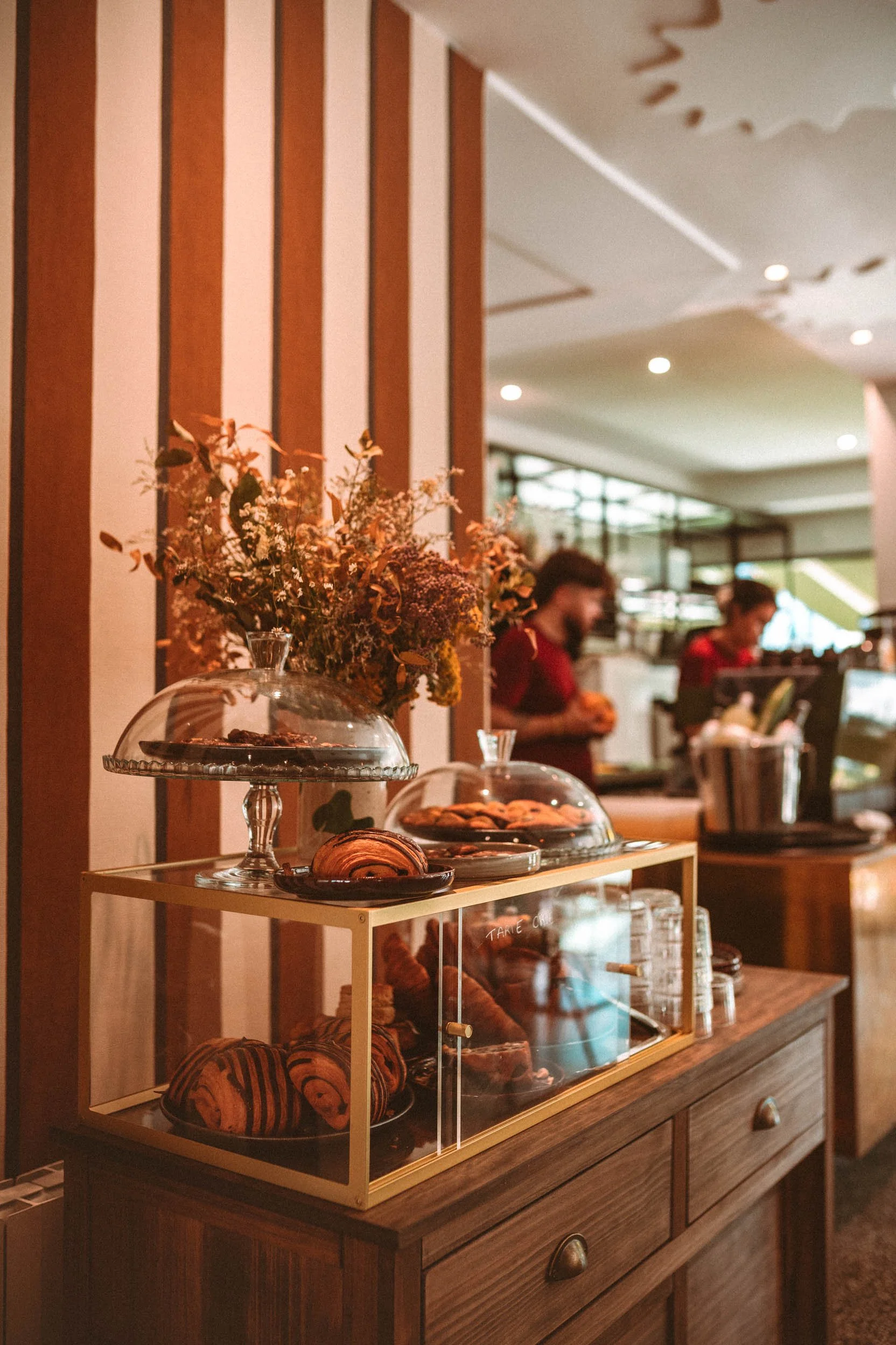 Vitrine avec des pâtisseries, croissants et cookies, décorée de fleurs séchées, dans un café ou un restaurant.