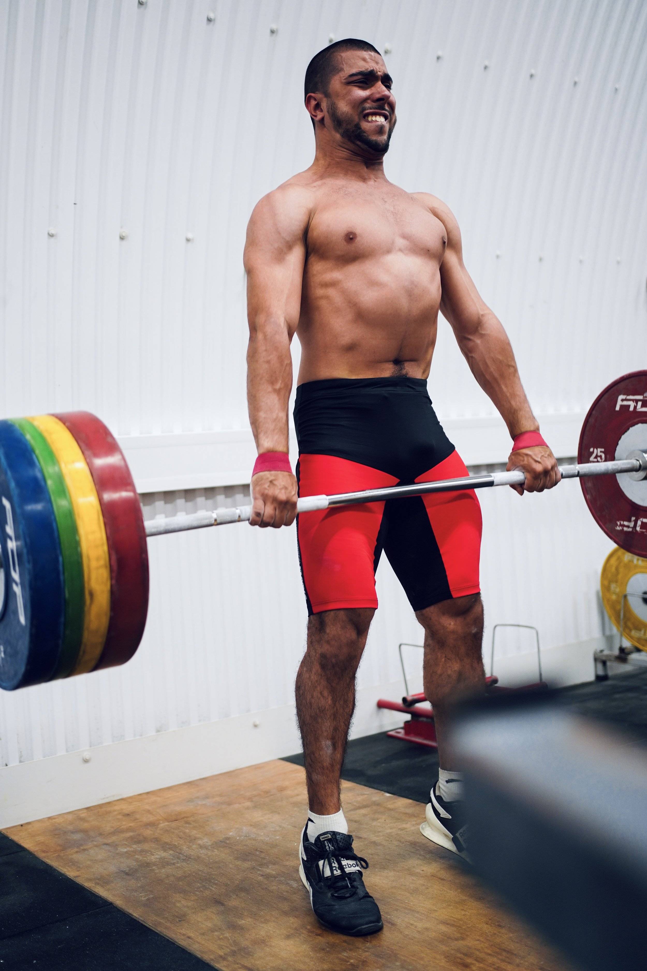 A shirtless man lifting a heavy barbell in a gym, displaying effort and strength.