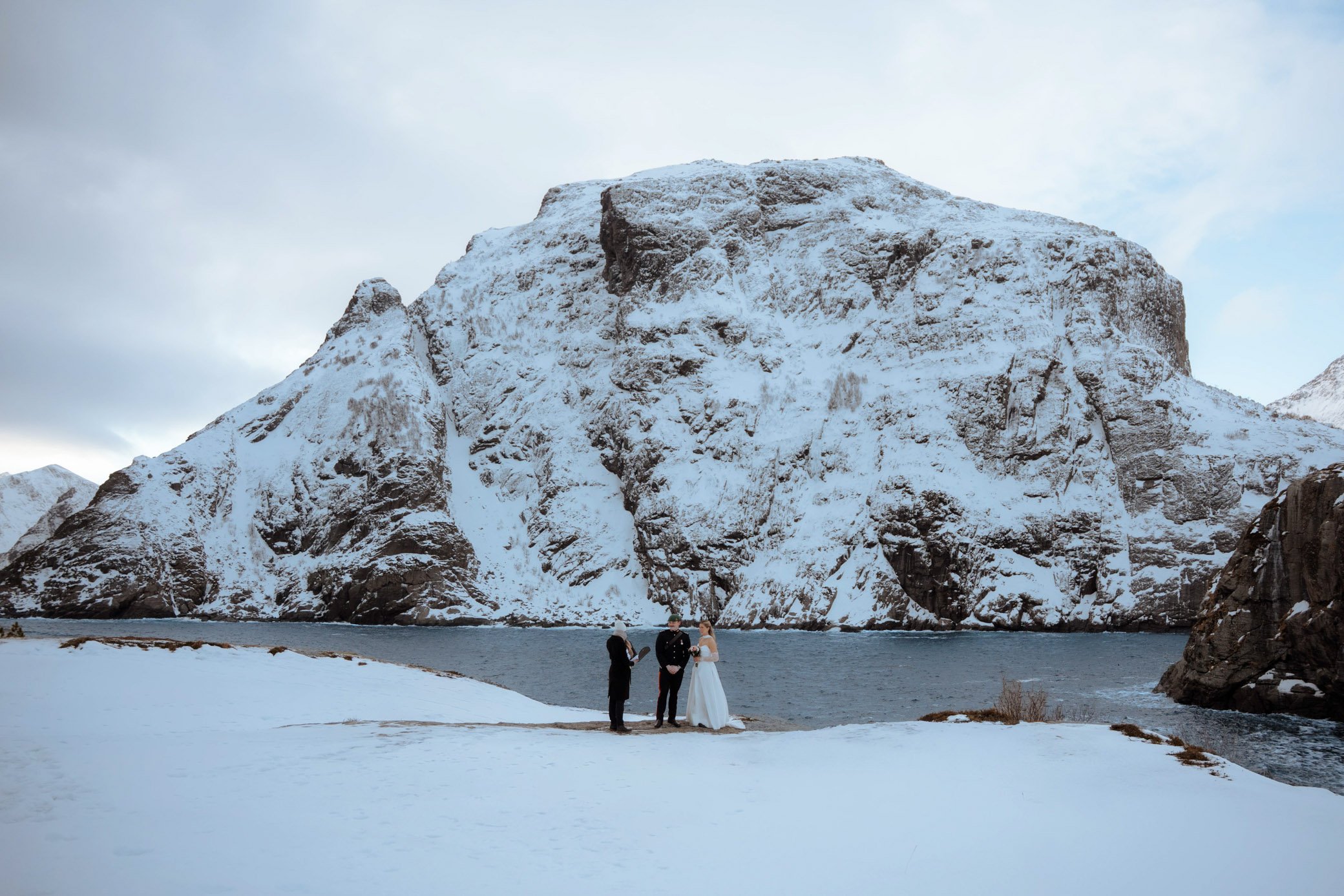 Couple during winter elopement on dramatic cliffs in Å Lofoten with snowy mountain backdrop in Northern Norway
