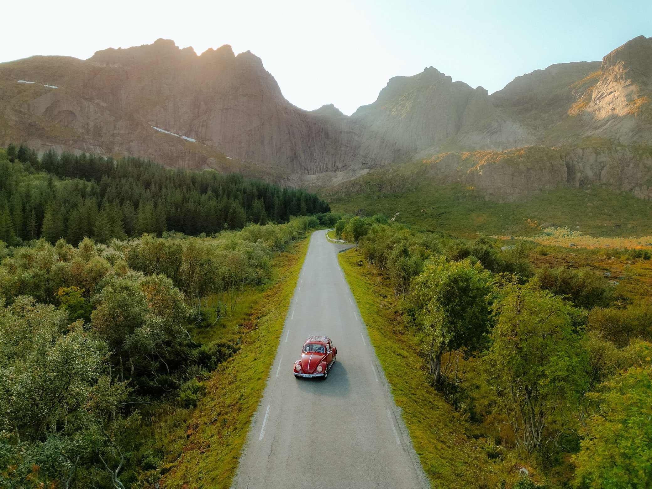 Couple driving red VW Käfer on scenic road in Lofoten towards Nusfjord