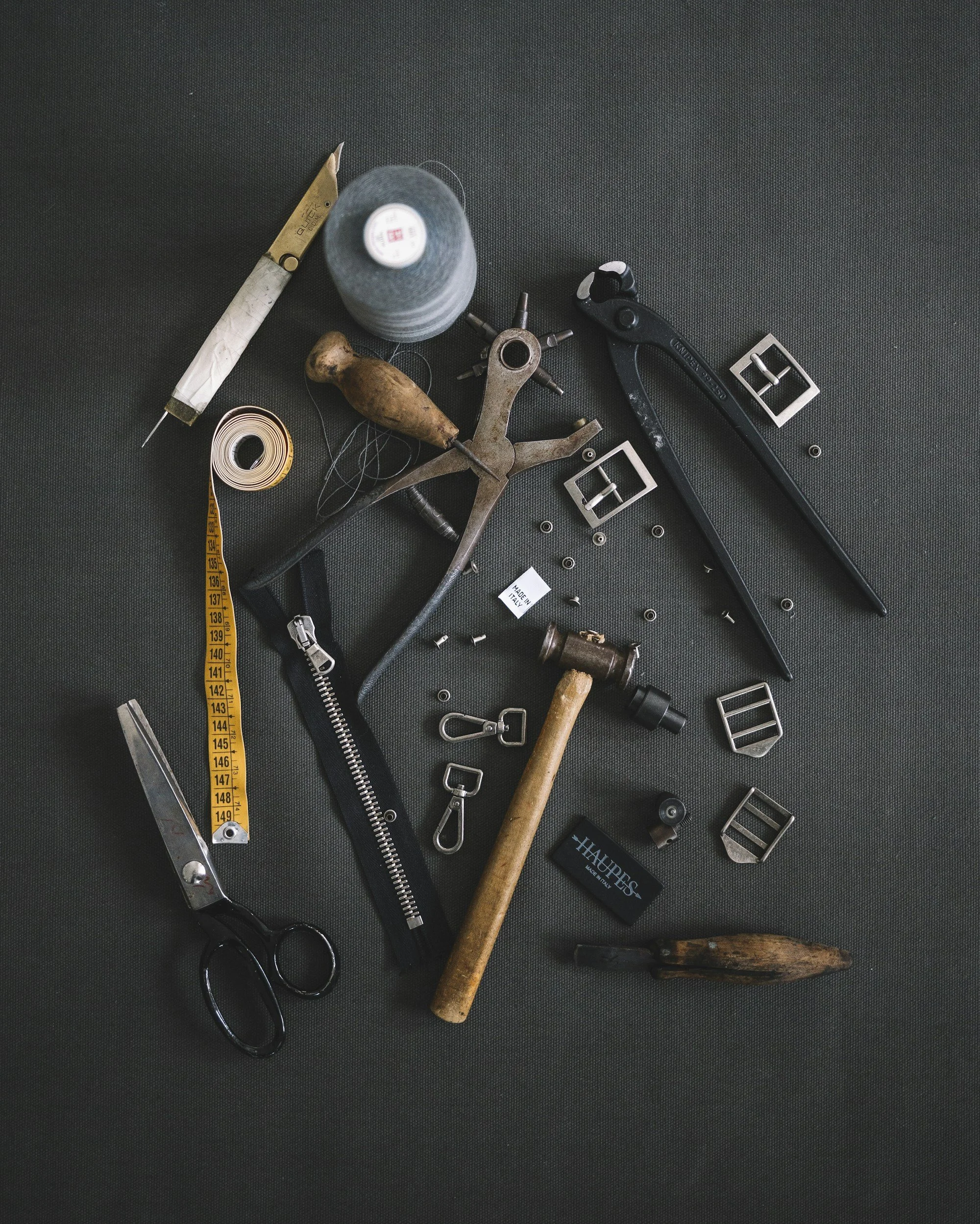 Various tools including scissors, a hammer, wrenches, buckles, a measuring tape, screws, nails, and a screwdriver scattered on a dark surface.