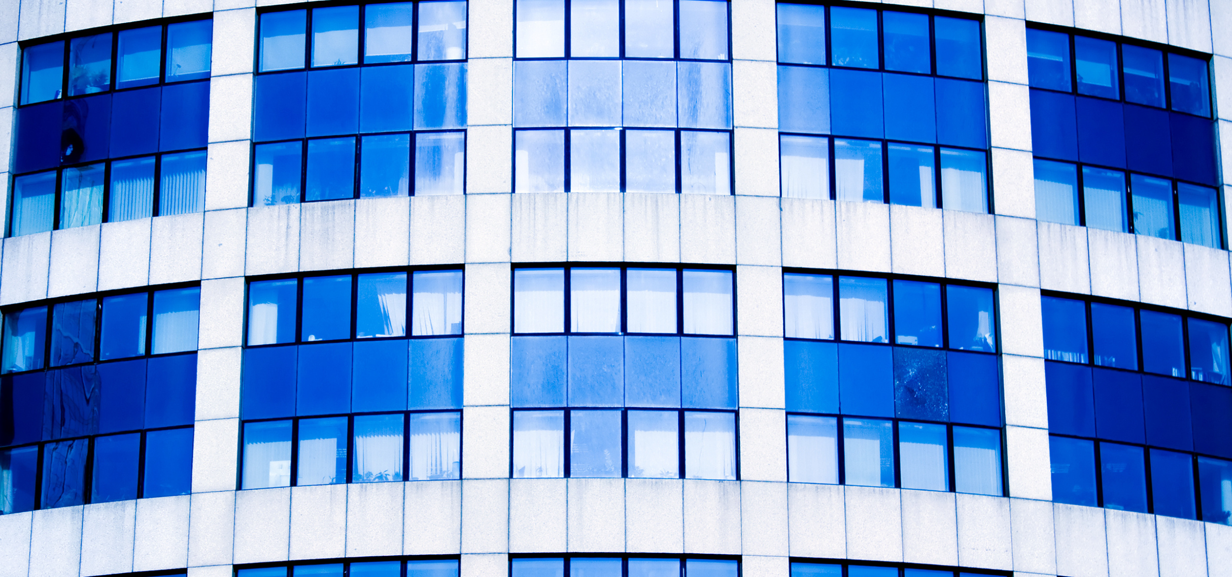 Close-up of a modern office building with curved glass windows and white concrete panels.