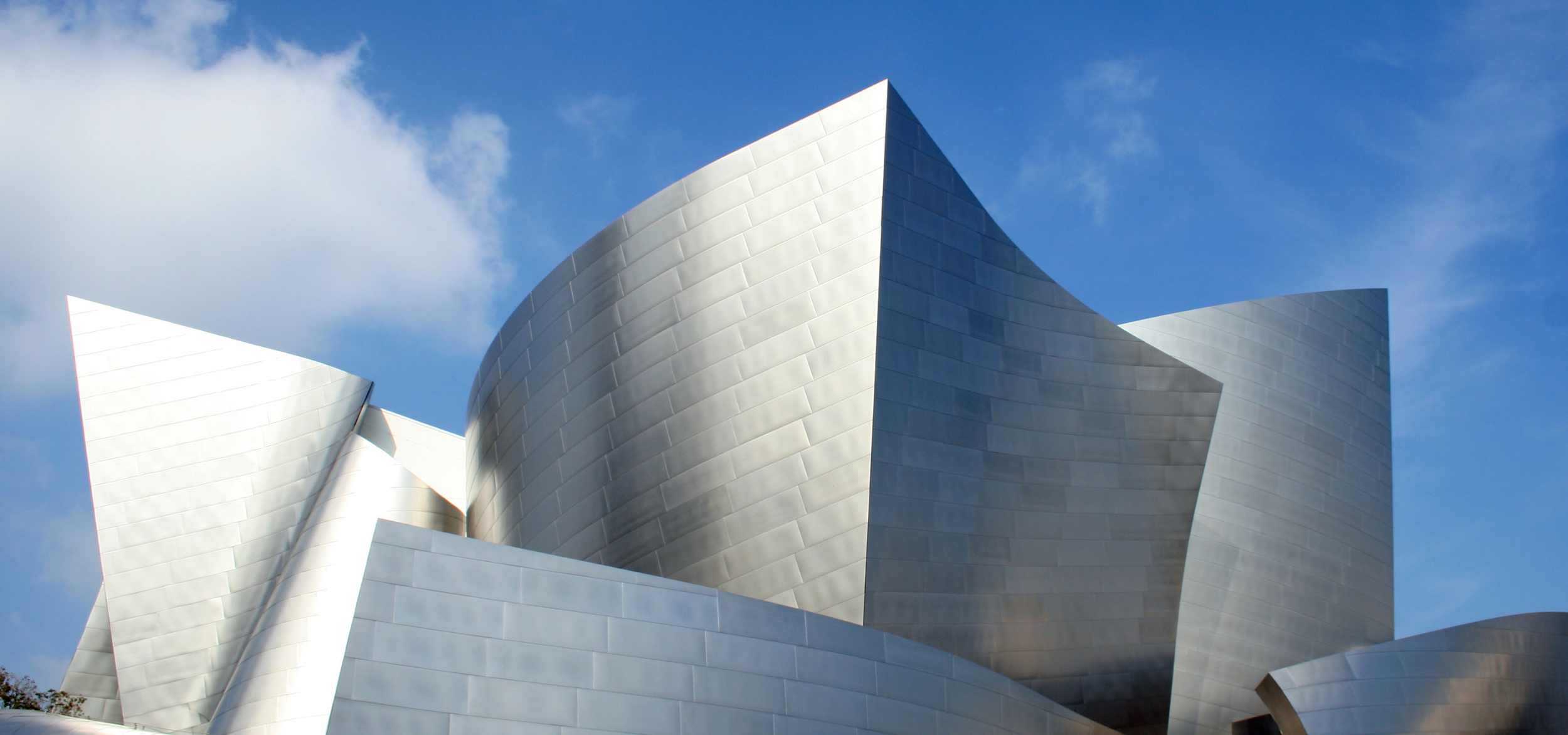 Close-up view of a modern, abstract building with metallic silver walls and curved shapes against a blue sky with some clouds.