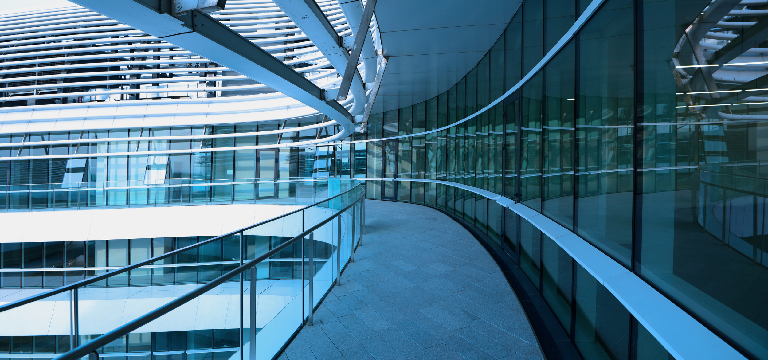 Modern building with curved glass walls, metal framework, and balcony railings in an urban setting.