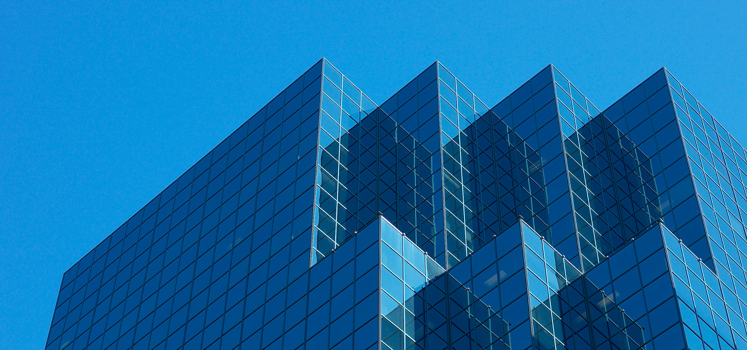 A modern glass skyscraper with a reflective exterior against a clear blue sky.