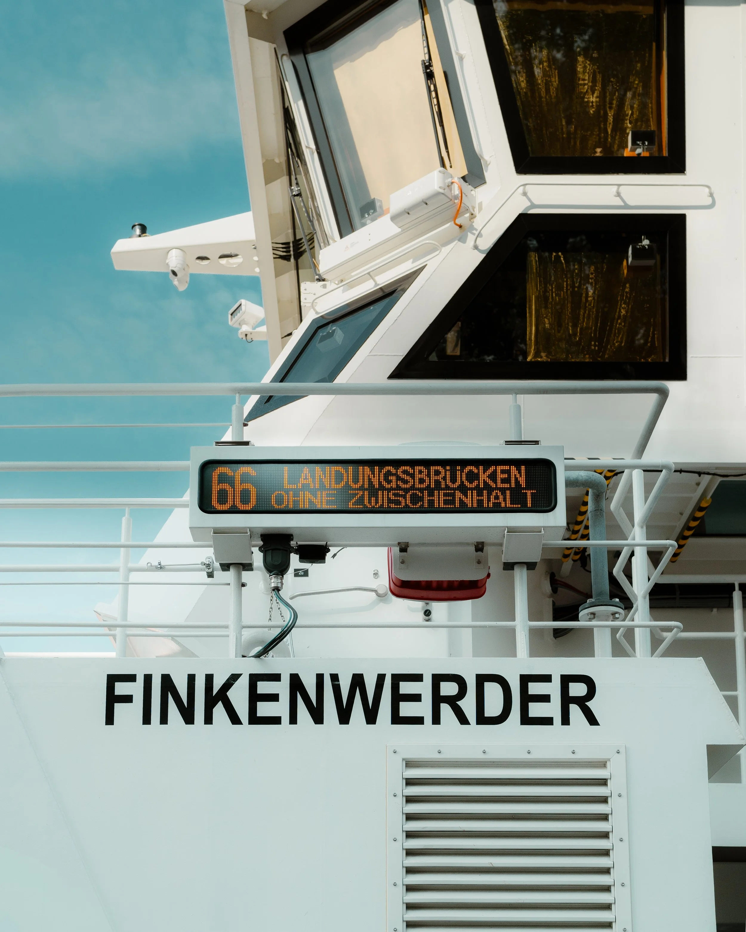 Close-up of the front of a white ferry boat named Finkenwerder, displaying a digital sign with route information for route 66 to Landungsbrücken, with a backdrop of a blue sky.