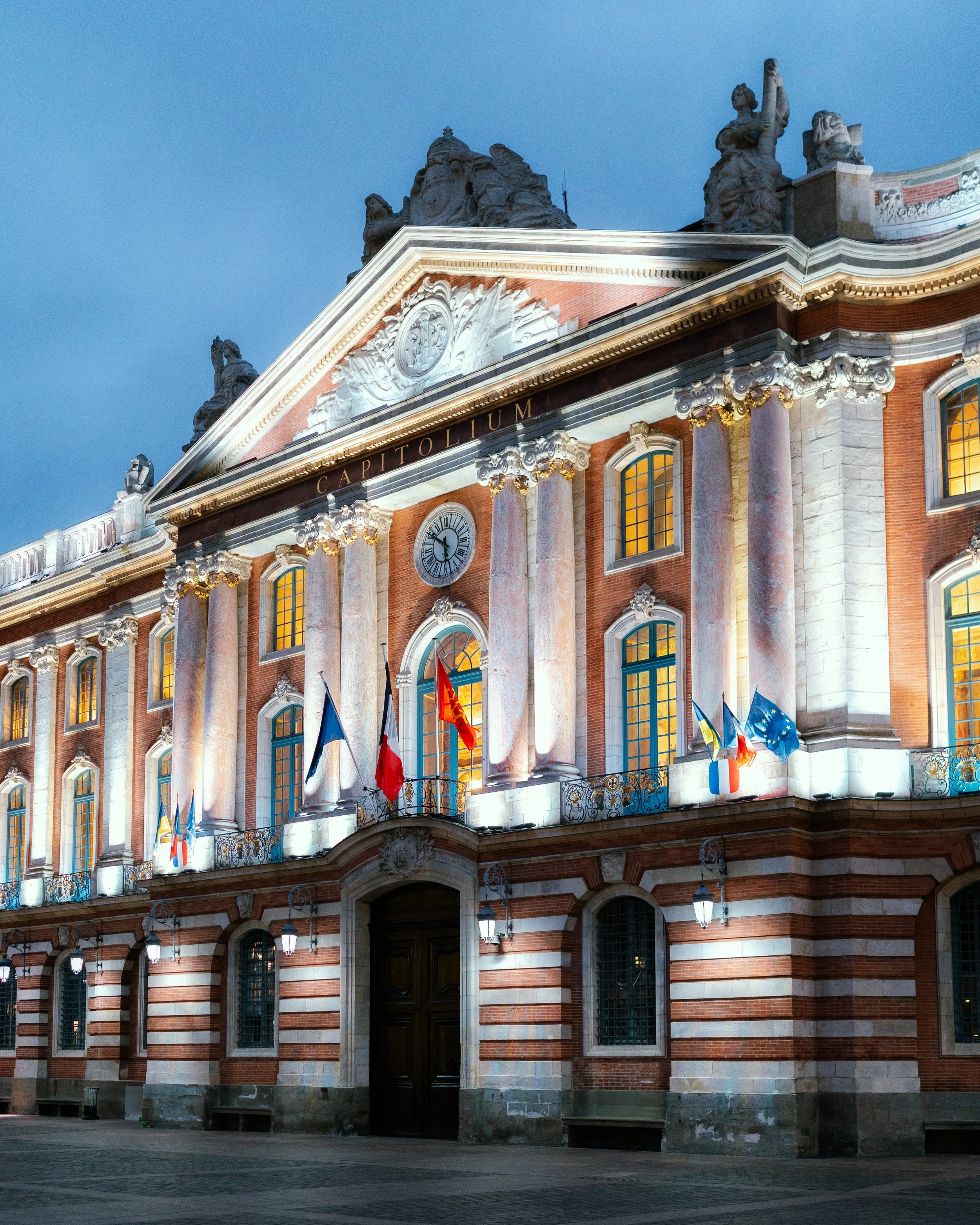 Night view of the illuminated front of the Palais Bourbon, the French National Assembly building, with flags displayed above the entrance.