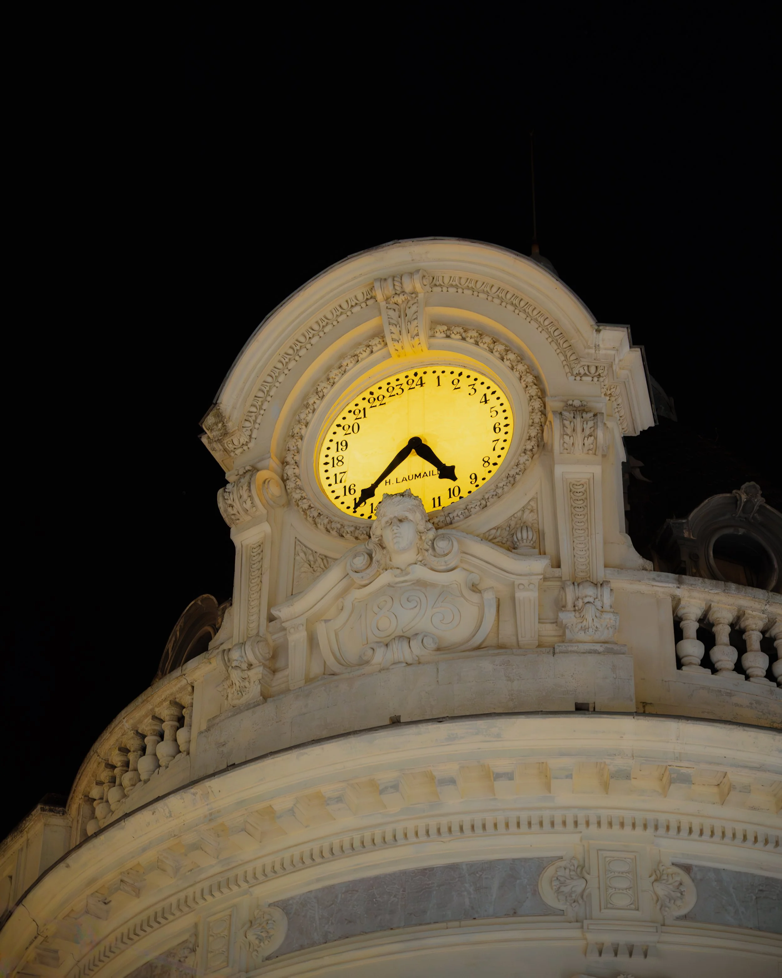 A historic clock tower illuminated at night, showing the time as 10:44, with decorative architectural details and the year 1895 engraved on the building.