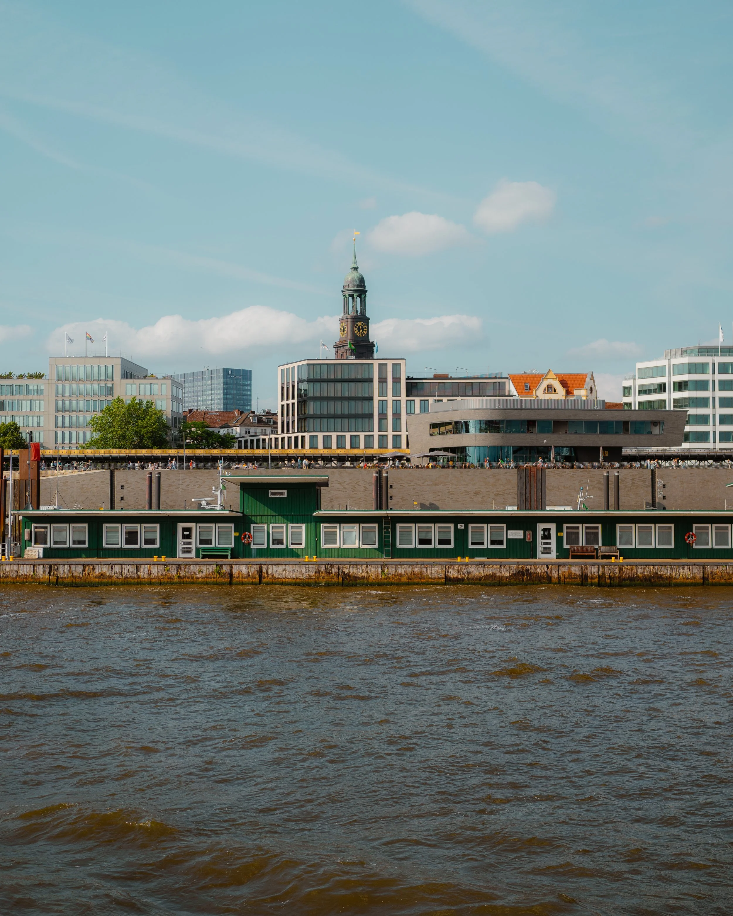 City skyline with modern buildings, a clock tower, and a waterfront houseboat on a river.