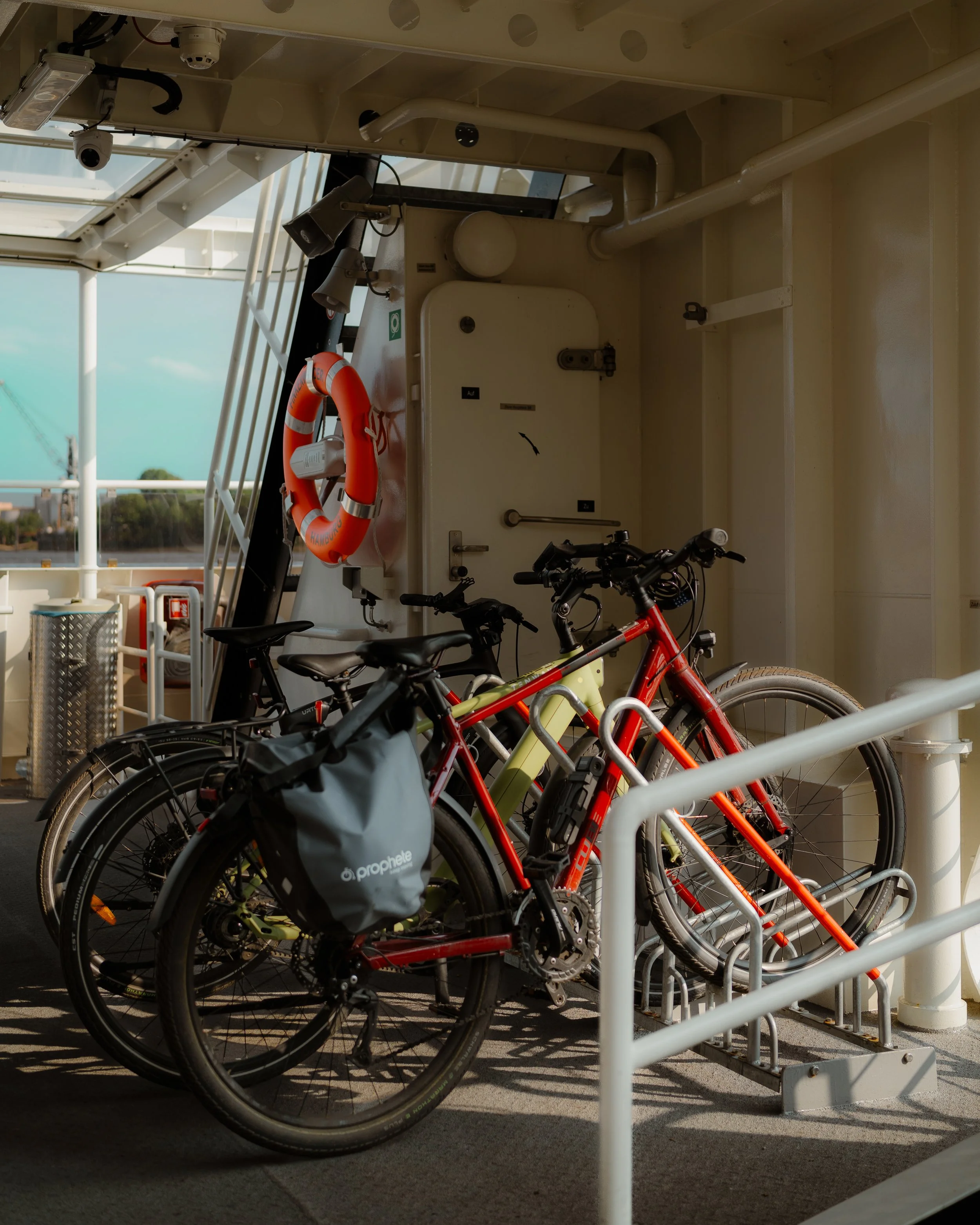 Bicycles parked on a ferry deck with white railings and a view of the water and sky in the background.