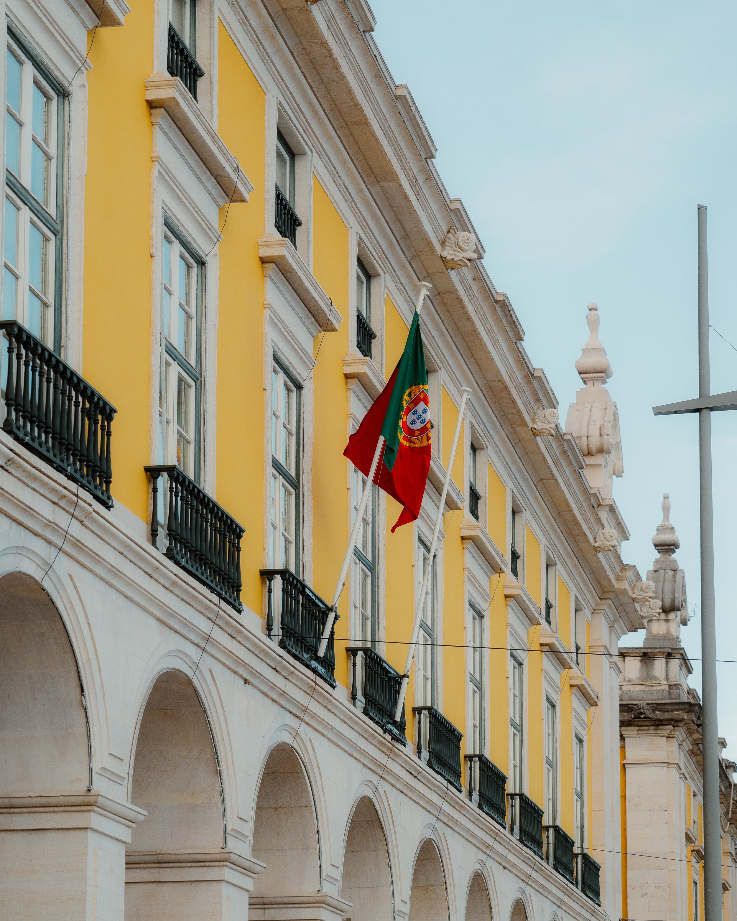 Yellow building with arched windows and black balconies, Portuguese flag hanging from pole.