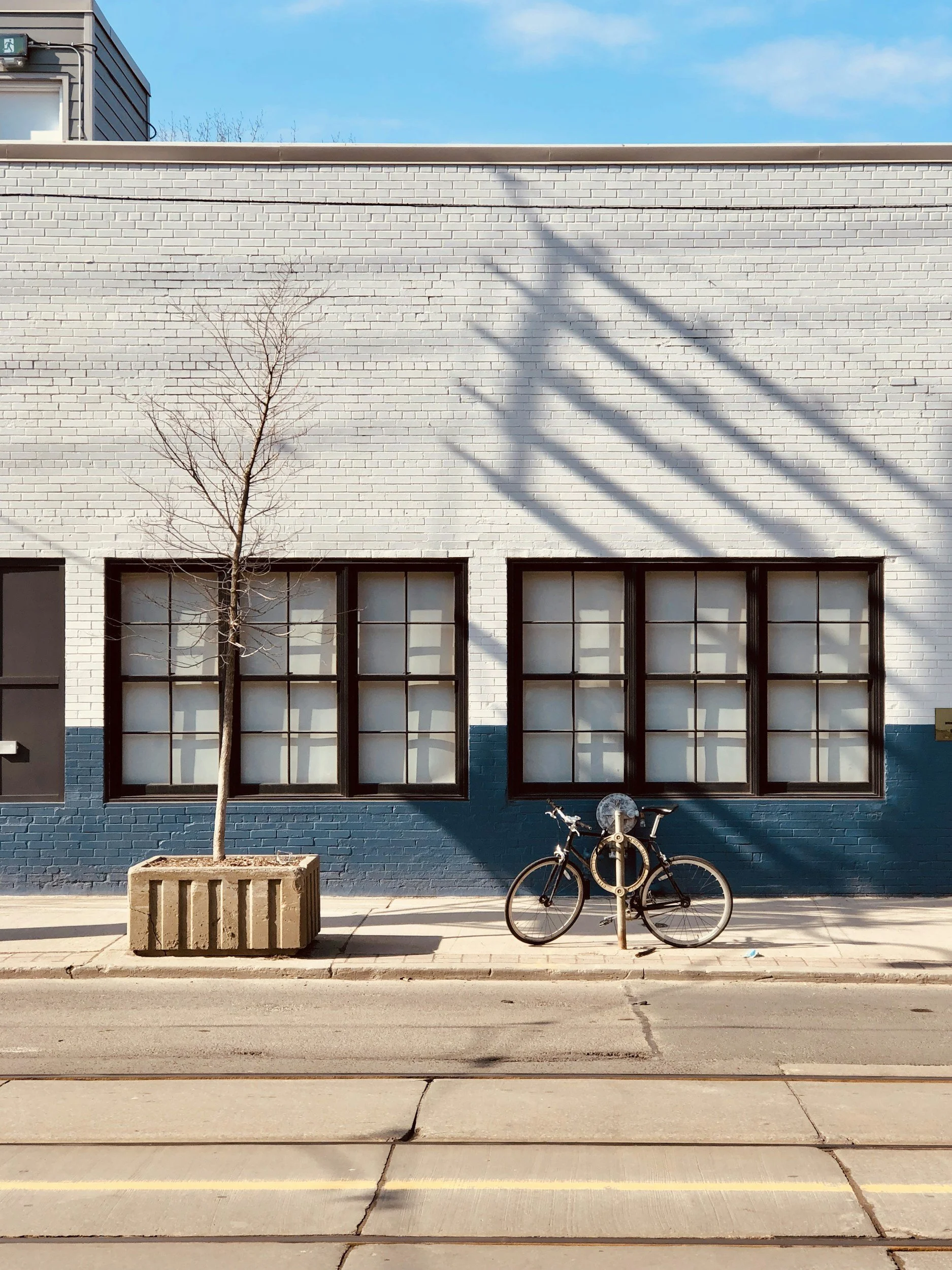 A bicycle locked up in front of a white brick building on a quiet city street, a grounded moment of everyday urban life