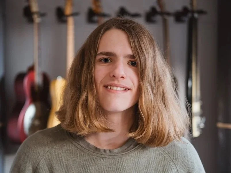 Junge Frau mit mittellangen braunen Haaren vor Gitarren im Hintergrund.