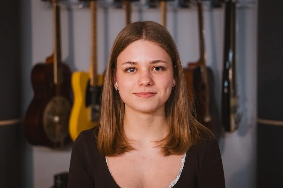 Junge Frau mit braunen Haaren vor Gitarren im Musikraum
