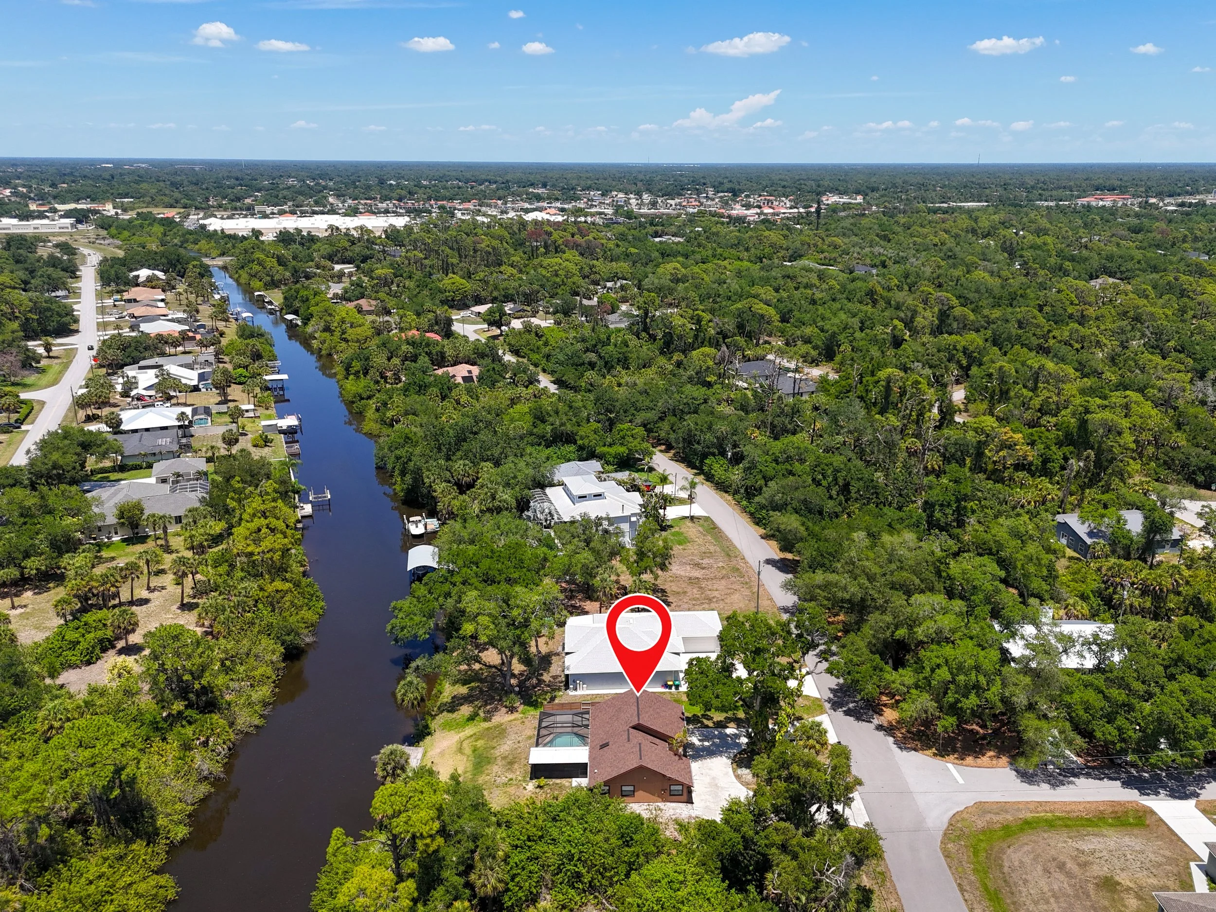 Aerial view of a residential neighborhood with houses, trees, and a water canal, under a partly cloudy sky.