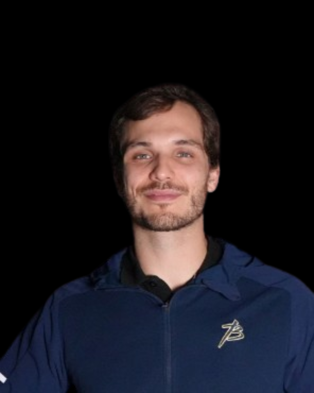 A young man with dark hair and facial hair, smiling, wearing a blue jacket with a logo on the chest, against a black background.