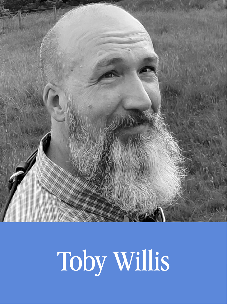 A black and white portrait of a smiling man with a beard and mustache, wearing a checkered shirt, outdoors in a grassy area. The image has a blue banner at the bottom with the name "Toby Willis".