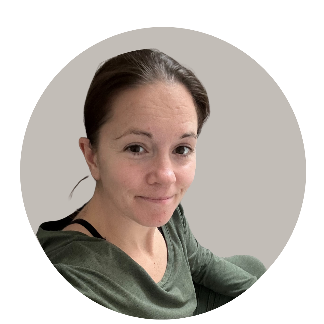 A woman with short brown hair and a slight smile, wearing a green top, sitting against a gray background.