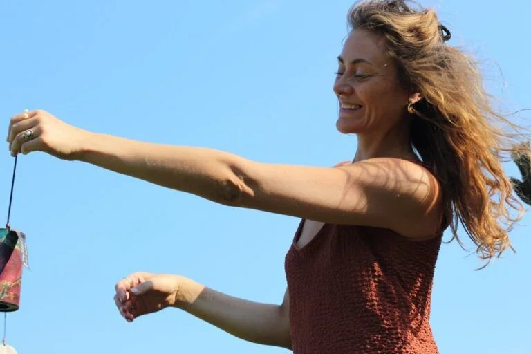 A woman with curly red hair smiling and holding a kite string outdoors on a sunny day.
