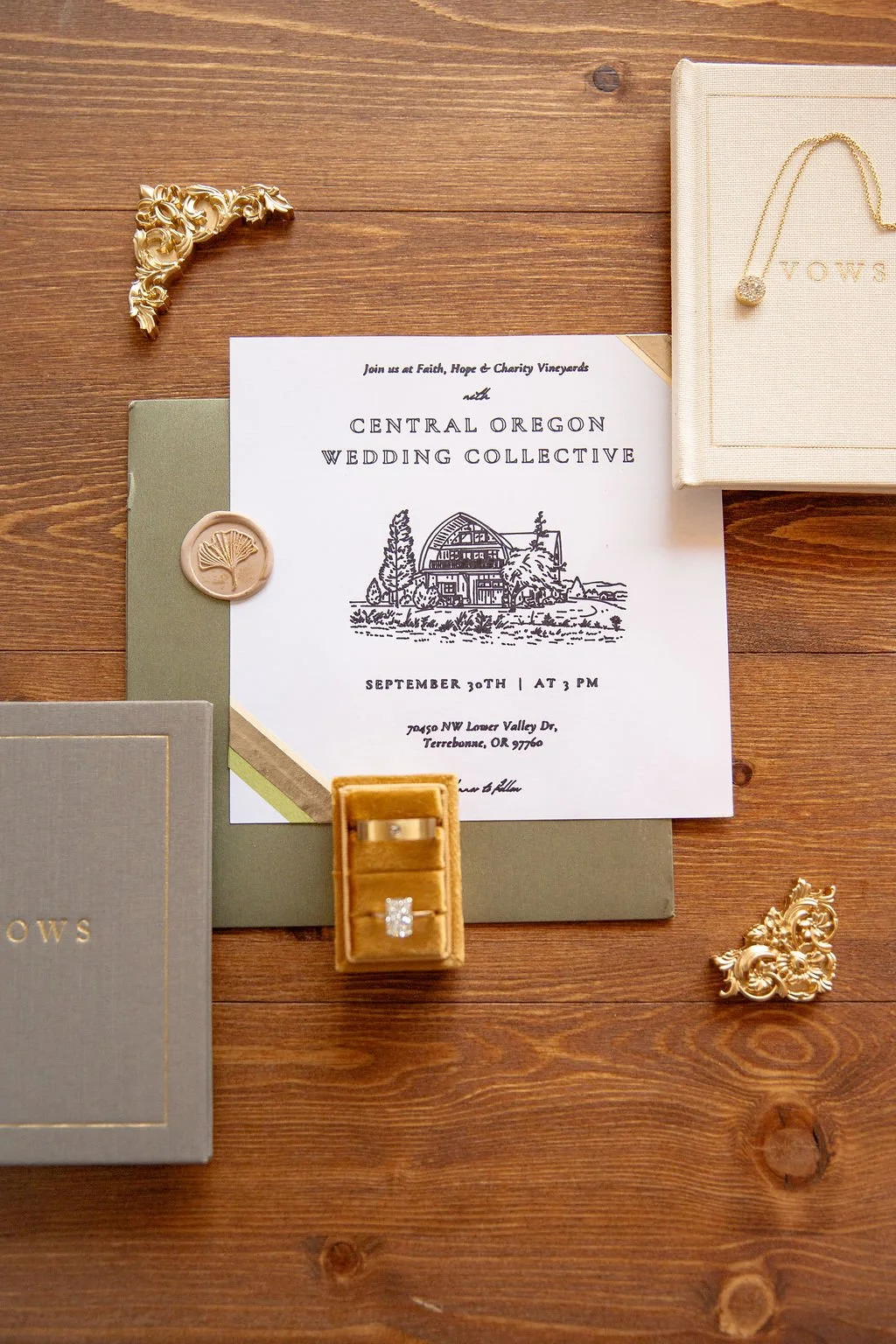Wedding invitation with gold decorative items, jewelry, and a ring, all arranged on a wooden table.