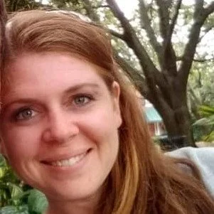 A pretty Caucasian woman with long honey-blonde hair leaning against a tree