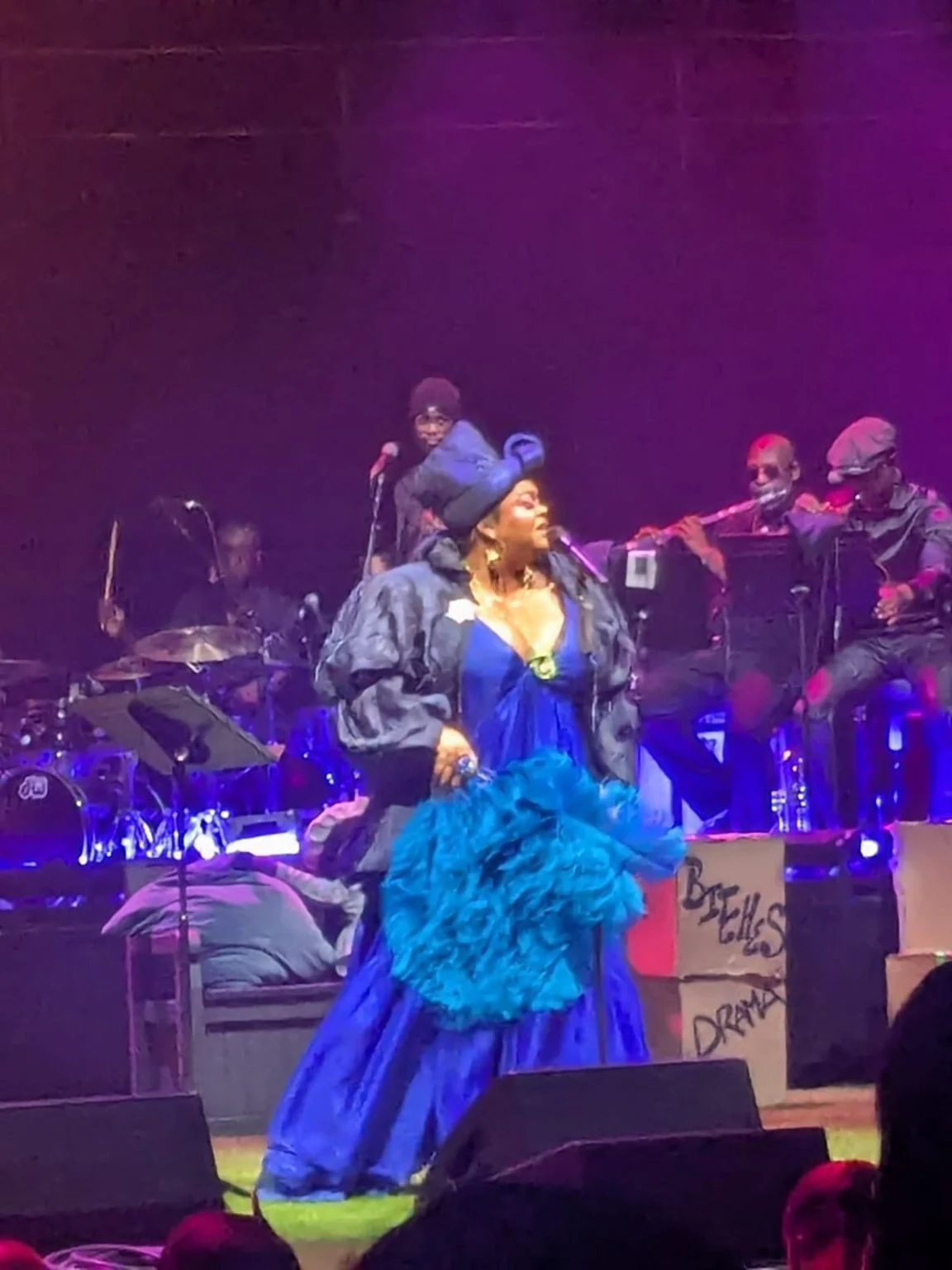 Jill Scott performing on stage in blue, with her band behind her.